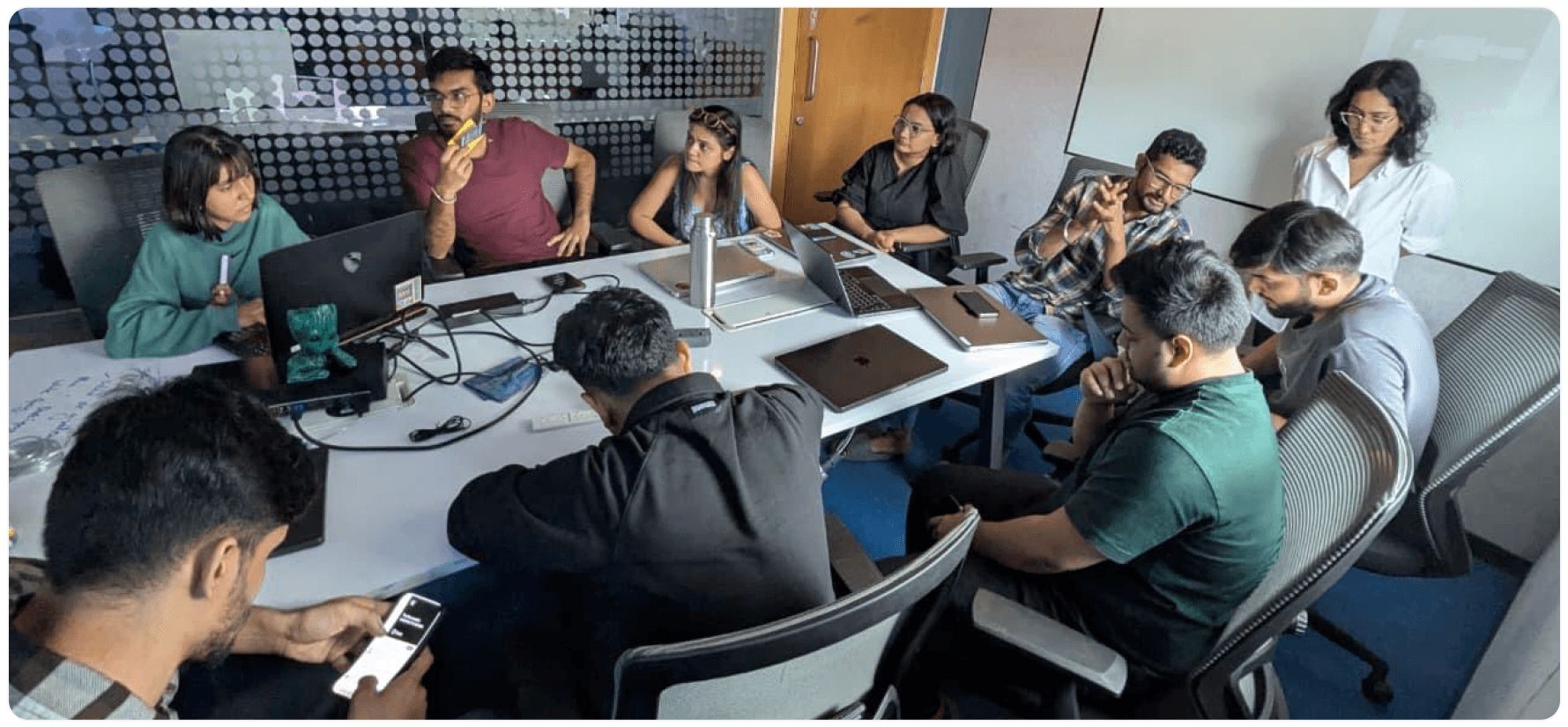 A team of engineers and designers gathered around a table with laptops open, in discussion